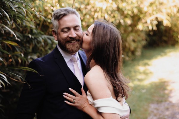 Bride kisses groom on cheek in garden