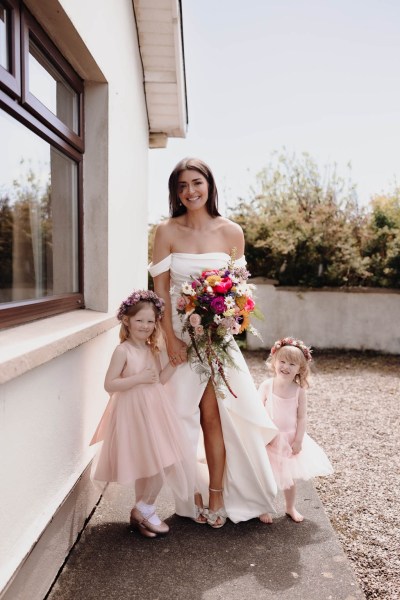 Bride and her daughter two little girls pose for a photo outside of house