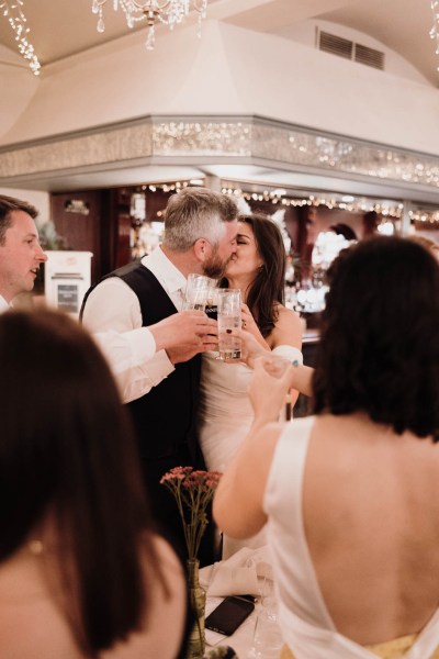 Bride groom and guests at dining room table groom gives bride a kiss