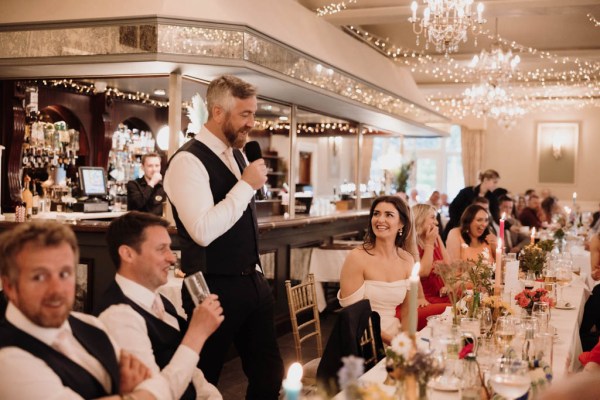 Bride groom and guests at dining room table groom gives a speech