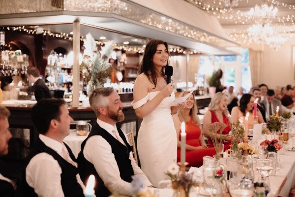 Bride groom and guests at dining room table she gives a speech