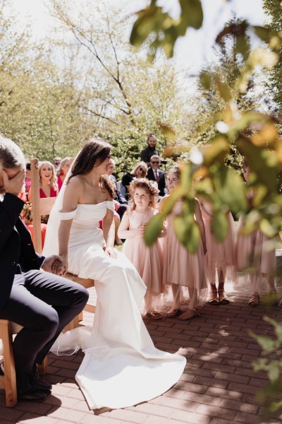 Bride and groom seated before celebrant during ceremony smiling laughing with little girls beside them