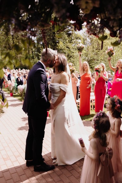 Bride groom little girls and bridesmaids in background during ceremony the couple kiss