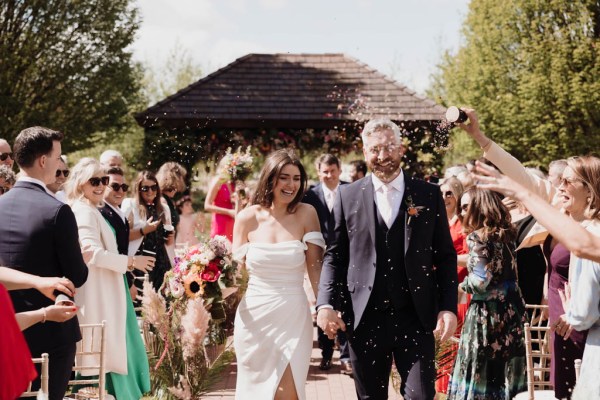 Bride and groom just wed leaving ceremony guests clap and celebrate confetti