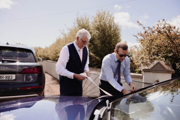 Family members readying the wedding car, placing ribbon on windshield wipers