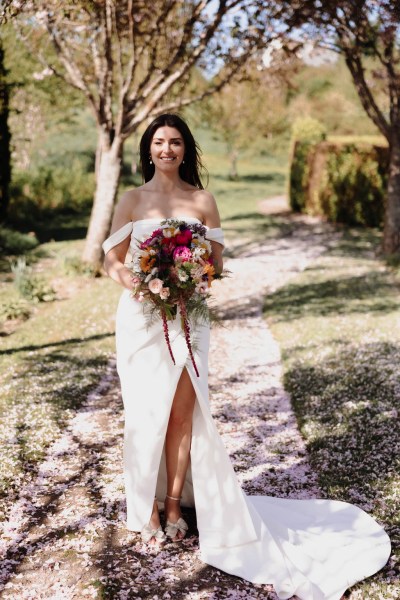 Bride on her own stands in garden holding bouquet flowers smiling