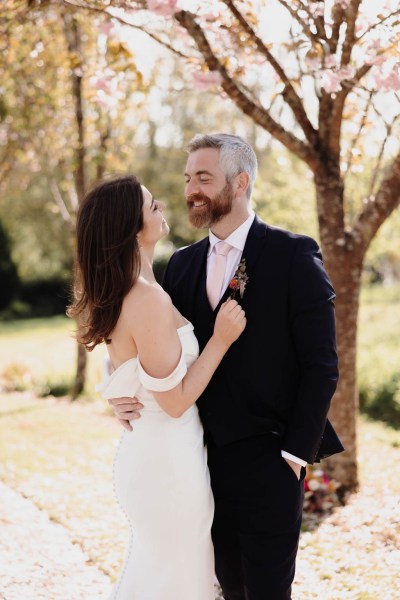 Bride and groom stand in the garden smiling facing each other