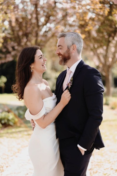 Bride and groom stand in the garden smiling facing each other