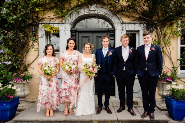 Bride groom bridesmaids and groomsmen pose outside of venue