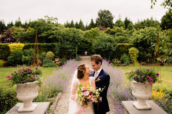 Bride and groom pose on pathway to wedding venue in garden they look at each other