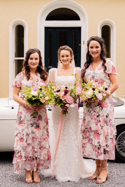 Bridesmaids and bride pose in front of white wedding car