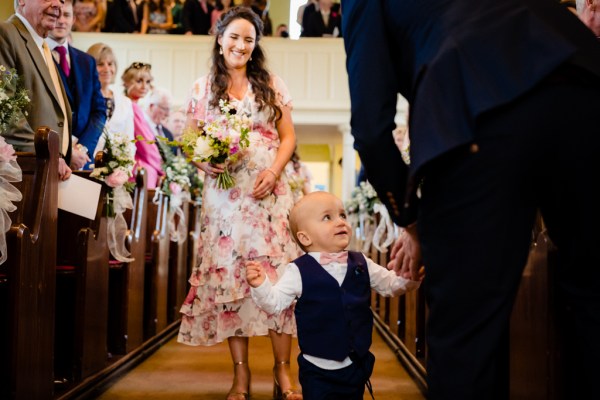 Little boy in suit and bridesmaid behind him