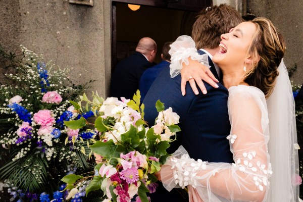 Bride and groom smile laughing holding bouquet flowers