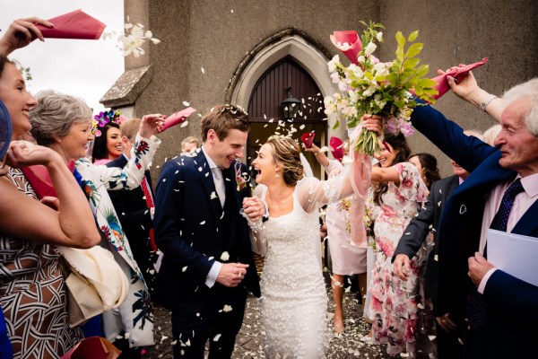 Bride and groom exit church confetti is being thrown over them by guests