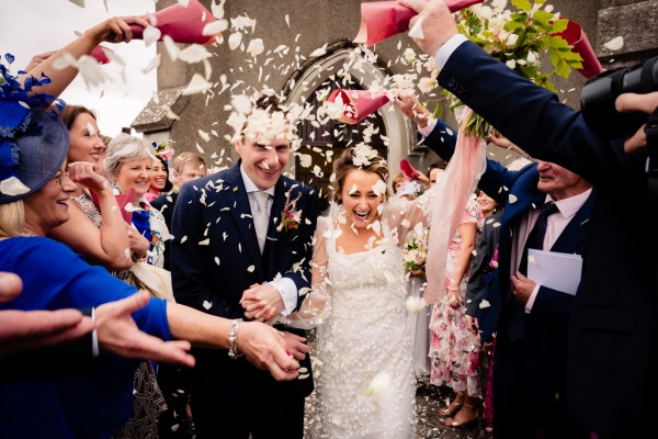 Bride and groom exit church confetti is being thrown over them by guests