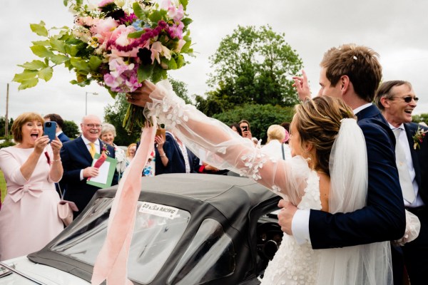 Bride and groom bouquet in the air with guests clapping