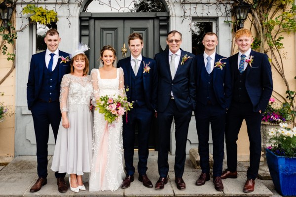 Mother father bride groom groomsmen pose for a photo