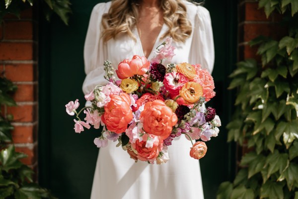 Bride on her own holding orange bright flower bouquet close up