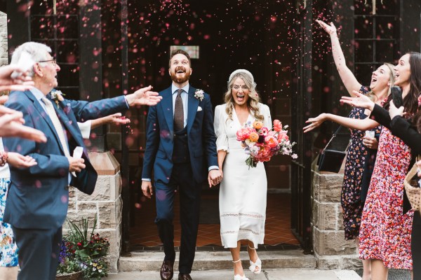 Bride and groom exit church they have confetti thrown over them by guests outside