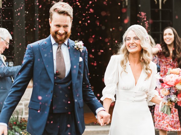 Bride and groom exit church they have confetti thrown over them by guests outside