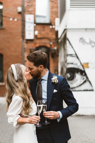 Bride and groom cheers with glasses of champagne/prosecco they kiss