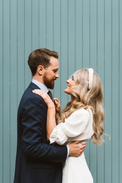 Green background bride puts her hands around groom as they hug