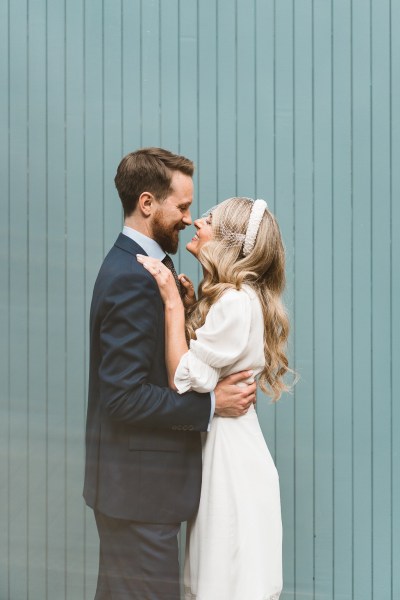 Green background bride puts her hands around groom as they hug