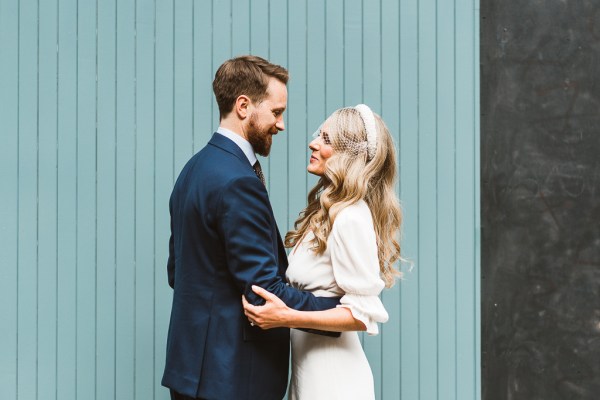 Green background bride puts her hands around groom as they hug