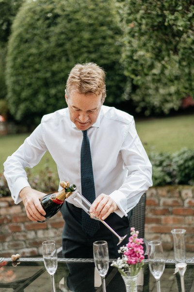 Father opens bottle of champagne pours it into glass