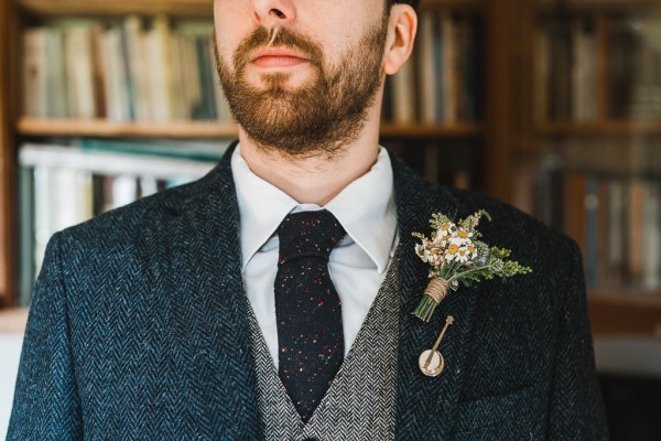 Groom smiles facing camera wearing suit and brooch