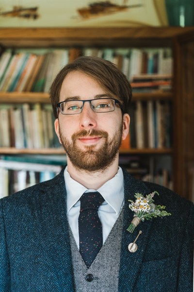 Groom smiles facing camera wearing suit and brooch