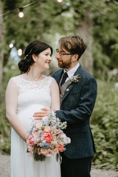 Groom looks at bride as he places hand on her pregnant belly