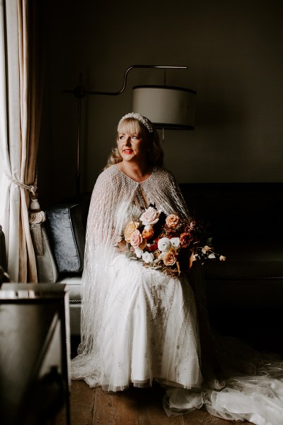 Bride holds bouquet of flowers on lap and looks out of window