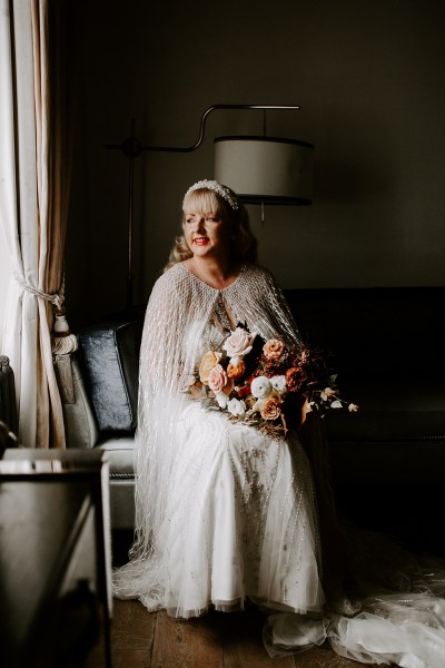 Bride holds bouquet of flowers on lap and looks out of window