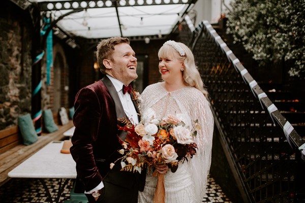 Groom chats with his bride wife on the cheek as she holds bouquet they laugh together