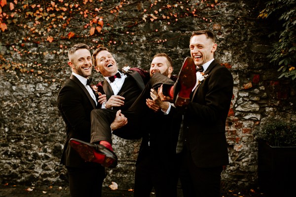 Groomsmen carry hold up groom and pose for a photo