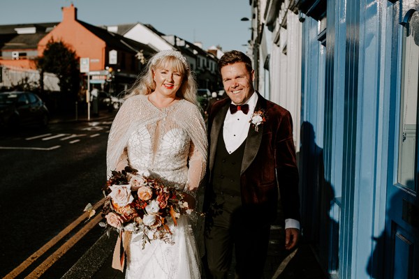 Bride and groom walk down pathway in sunshine all smiles