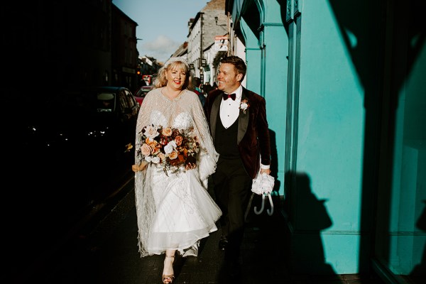 Bride and groom walk in the sunshine green painted wall