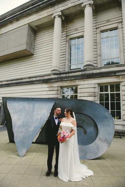 Bride and groom look at each other standing in front of statue