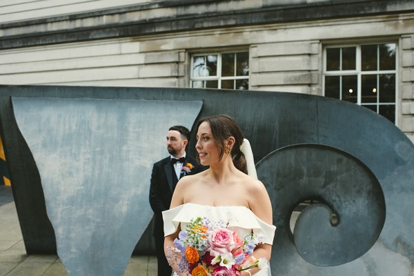 Bride, focus is on the colourful flowers groom in background