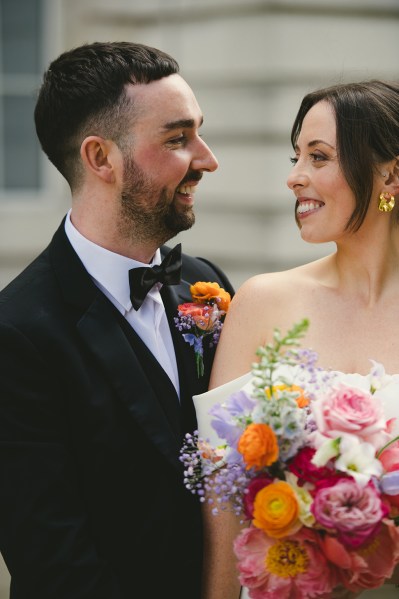 Bride and groom look at each other she holds colourful bouquet flowers