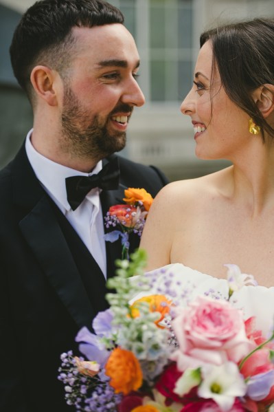 Bride and groom look at each other she holds colourful bouquet flowers