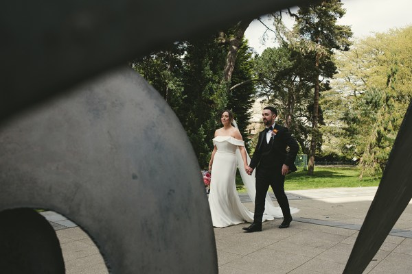 Bride and groom walk hand in hand in park