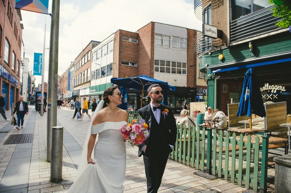 Bride and groom holding flowers walking along street