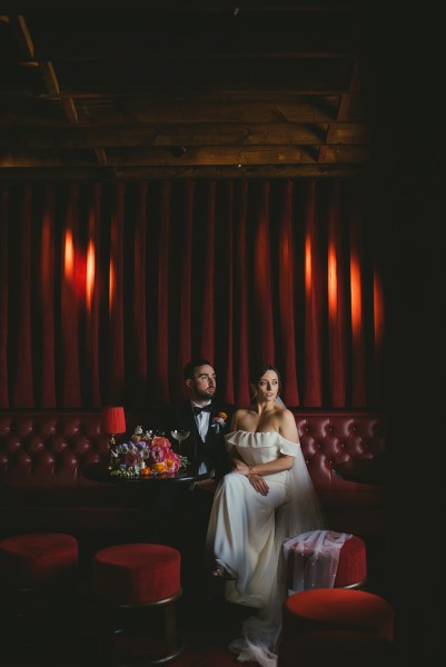 Bride and groom cocktail bar flowers seated on red leather couch