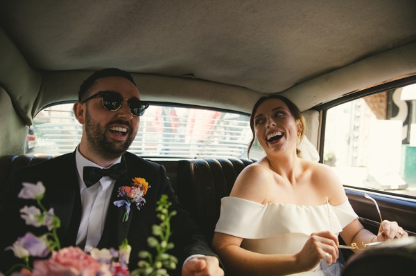 Bride and groom laughing in wedding car together