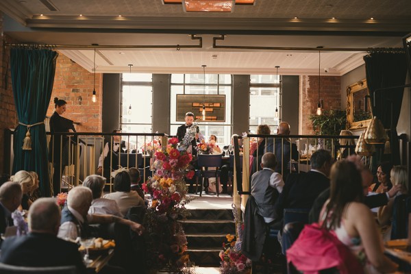 Guests seated in bar setting guests onlooking speeches bride and groom