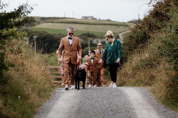 Groom black Labrador groomsmen and son walk down the road