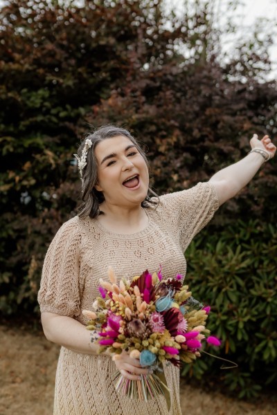 Bride stands holding bouquet flowers cheers hand in the air