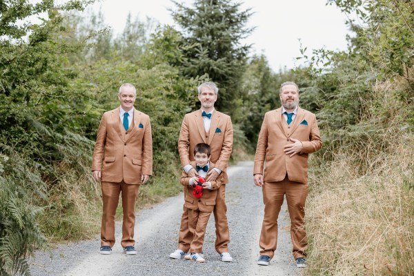 Groom and two groomsmen along with grooms son pose for a picture in brown suits